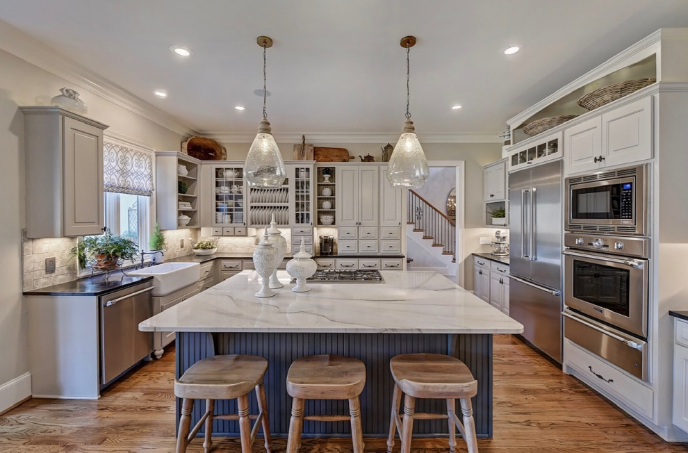 This is an example of a large eat-in kitchen in Charlotte with a farmhouse sink, raised-panel cabinets, beige cabinets, quartzite benchtops, grey splashback, ceramic splashback, stainless steel appliances, medium hardwood floors, with island, brown floor and white benchtop.