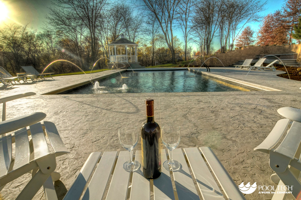 Example of a large mountain style backyard stamped concrete and rectangular pool fountain design in Cedar Rapids