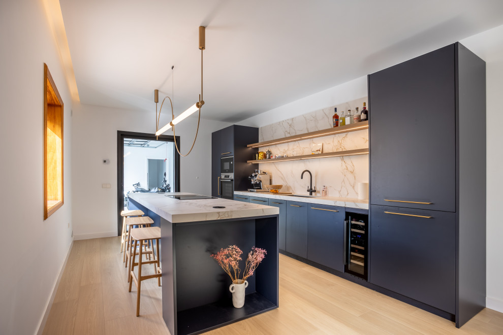 Photo of a large contemporary galley kitchen in Other with an undermount sink, flat-panel cabinets, blue cabinets, beige splashback, stone slab splashback, black appliances, light hardwood floors, with island, beige floor and beige benchtop.