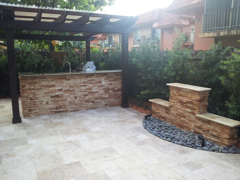 This is an example of a mid-sized contemporary backyard patio in Miami with an outdoor kitchen, natural stone pavers and a pergola.