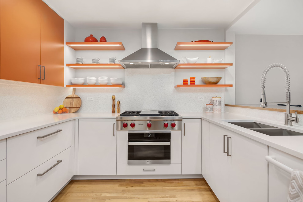 Photo of a mid-sized contemporary u-shaped kitchen in Chicago with a double-bowl sink, flat-panel cabinets, orange cabinets, white splashback, mosaic tile splashback, stainless steel appliances, medium hardwood floors, no island and brown floor.