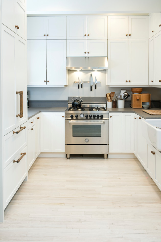 Photo of a mid-sized scandinavian u-shaped separate kitchen in Chicago with a farmhouse sink, shaker cabinets, white cabinets, quartz benchtops, grey splashback, stainless steel appliances, light hardwood floors and no island.