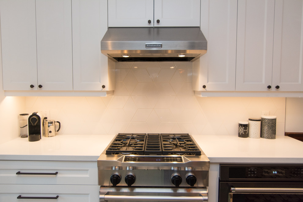 This is an example of a mid-sized transitional u-shaped eat-in kitchen in Toronto with flat-panel cabinets, white cabinets, quartz benchtops, white splashback, glass tile splashback, stainless steel appliances, ceramic floors and with island.