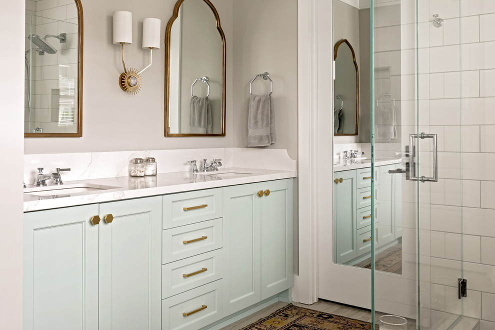 This is an example of a mid-sized transitional master bathroom in Charlotte with recessed-panel cabinets, turquoise cabinets, a freestanding tub, a corner shower, a two-piece toilet, white tile, ceramic tile, grey walls, porcelain floors, an undermount sink, engineered quartz benchtops, grey floor, a hinged shower door, white benchtops, an enclosed toilet, a double vanity, a built-in vanity and decorative wall panelling.