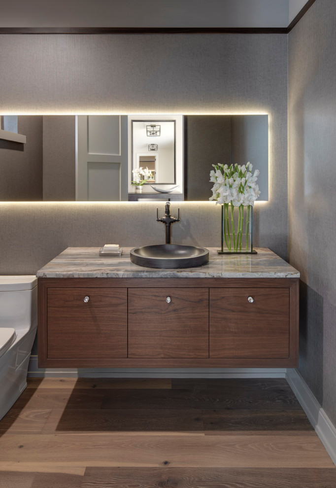 Photo of a midcentury powder room in Detroit with flat-panel cabinets, dark wood cabinets, a one-piece toilet, grey walls, light hardwood floors, a vessel sink, grey benchtops and wallpaper.