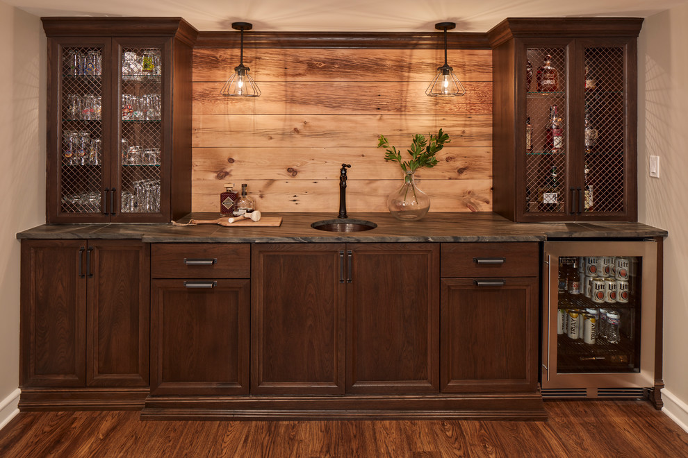 Traditional single-wall wet bar in Milwaukee with an undermount sink, recessed-panel cabinets, dark wood cabinets, timber splashback, brown benchtop and vinyl floors.