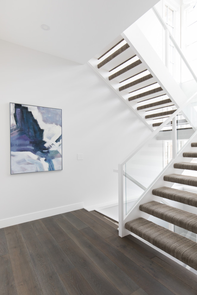 Пример оригинального дизайна: большая п-образная лестница в стиле неоклассика (современная классика) с ступенями с ковровым покрытием и стеклянными перилами