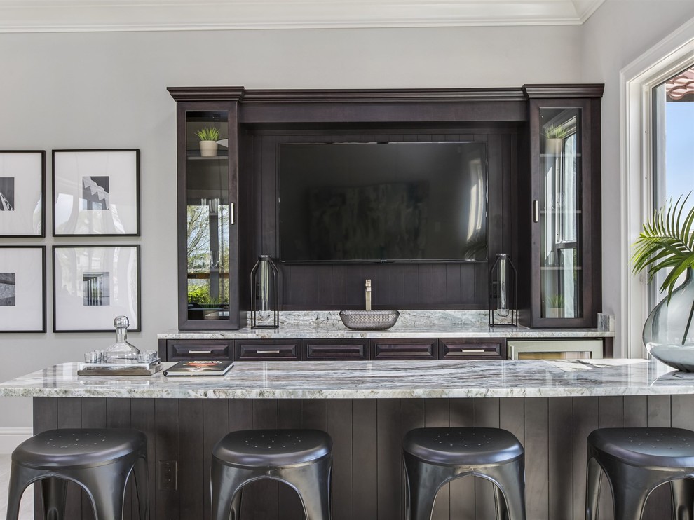 Mid-sized mediterranean galley seated home bar in Orlando with an undermount sink, glass-front cabinets, dark wood cabinets, granite benchtops, multi-coloured splashback, stone slab splashback and porcelain floors.