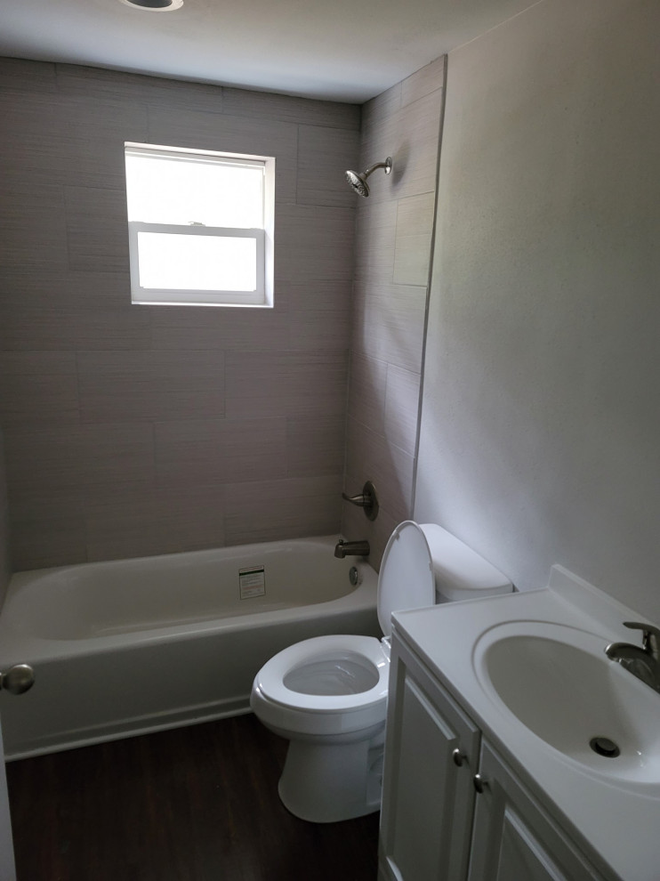 Идея дизайна: маленькая ванная комната в классическом стиле с фасадами с выступающей филенкой, белыми фасадами, накладной ванной, душем над ванной, унитазом-моноблоком, серой плиткой, керамической плиткой, серыми стенами, полом из ламината, монолитной раковиной, коричневым полом, шторкой для ванной, белой столешницей, тумбой под одну раковину и напольной тумбой для на участке и в саду