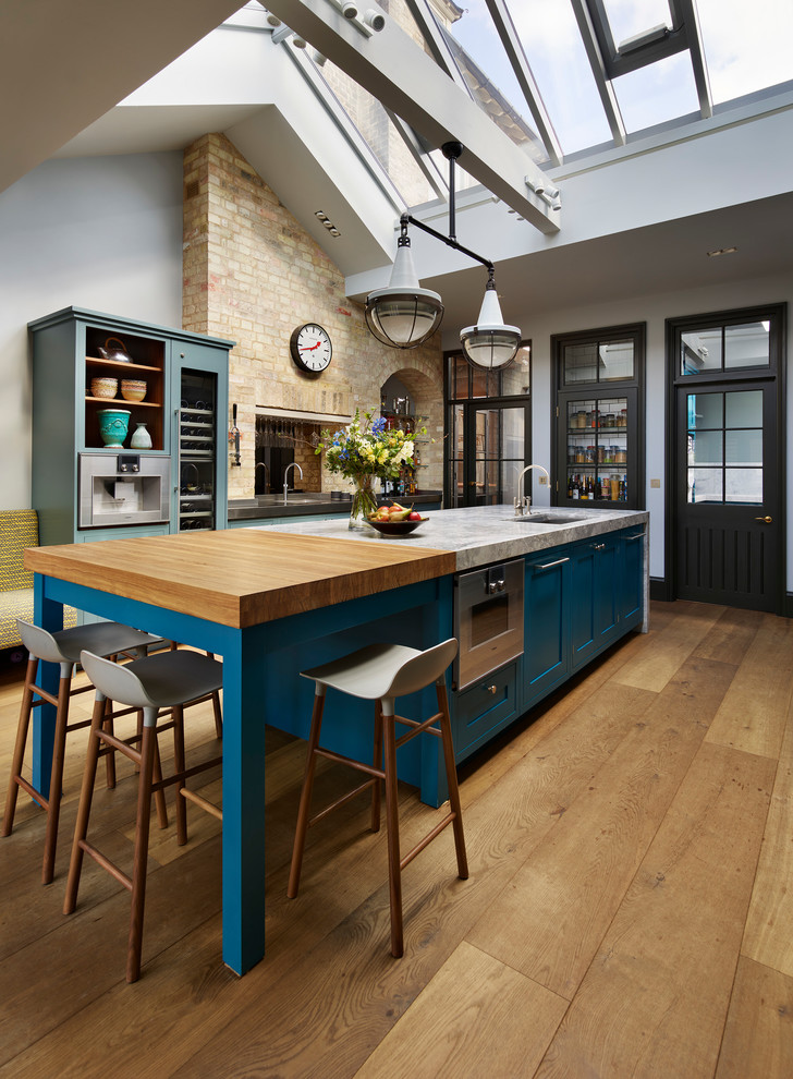 This is an example of a large transitional kitchen in London with an undermount sink, blue cabinets, medium hardwood floors, with island, shaker cabinets and wood benchtops.