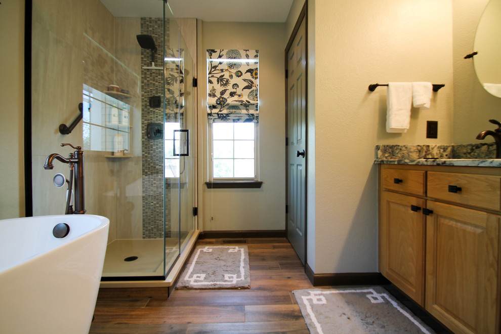 Design ideas for a mid-sized traditional master bathroom in Denver with raised-panel cabinets, light wood cabinets, a freestanding tub, a corner shower, a one-piece toilet, beige tile, porcelain tile, green walls, porcelain floors, an undermount sink, granite benchtops, brown floor and a hinged shower door.