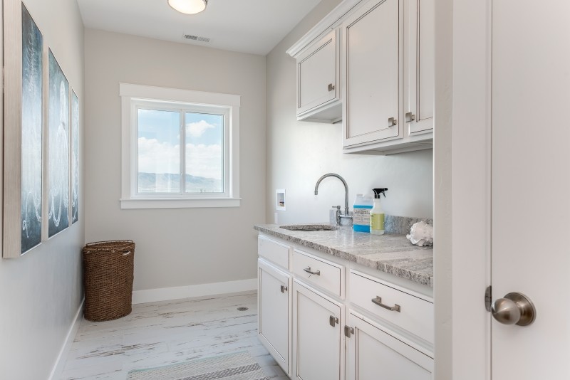 Mid-sized beach style single-wall dedicated laundry room in Salt Lake City with an undermount sink, shaker cabinets, white cabinets, granite benchtops, grey walls, ceramic floors, a side-by-side washer and dryer and white floor.