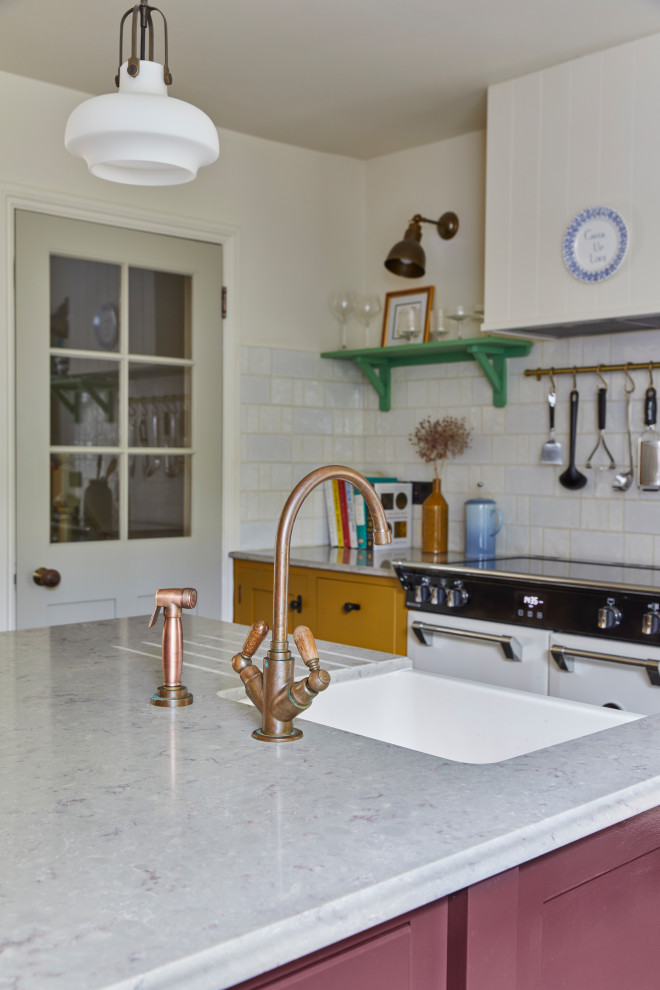This is an example of a large transitional eat-in kitchen in London with a farmhouse sink, shaker cabinets, yellow cabinets, marble benchtops, white splashback, ceramic splashback, white appliances, limestone floors, with island, black floor and brown benchtop.