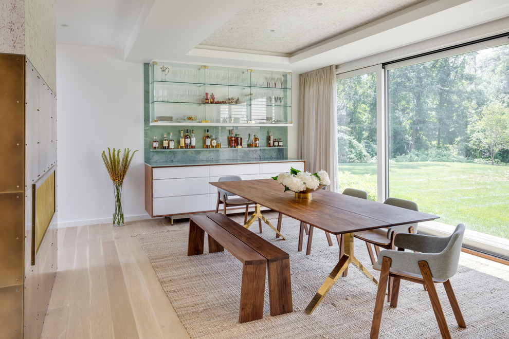 Photo of a mid-sized contemporary dining room in Boston with white walls, light hardwood floors, a two-sided fireplace, a metal fireplace surround and beige floor.