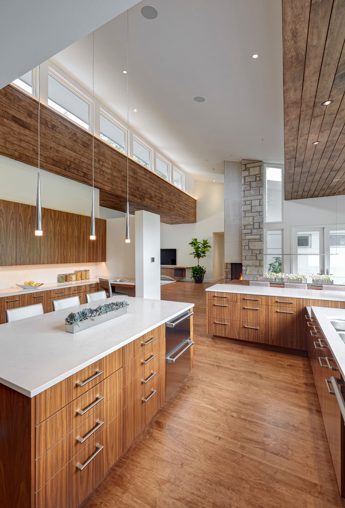 Photo of a large contemporary u-shaped eat-in kitchen in Detroit with a double-bowl sink, flat-panel cabinets, medium wood cabinets, quartzite benchtops, white splashback, stainless steel appliances, light hardwood floors, multiple islands and beige floor.