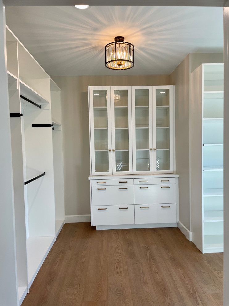 Design ideas for a large traditional storage and wardrobe in Orange County with white cabinets, flat-panel cabinets, laminate floors and brown floor.