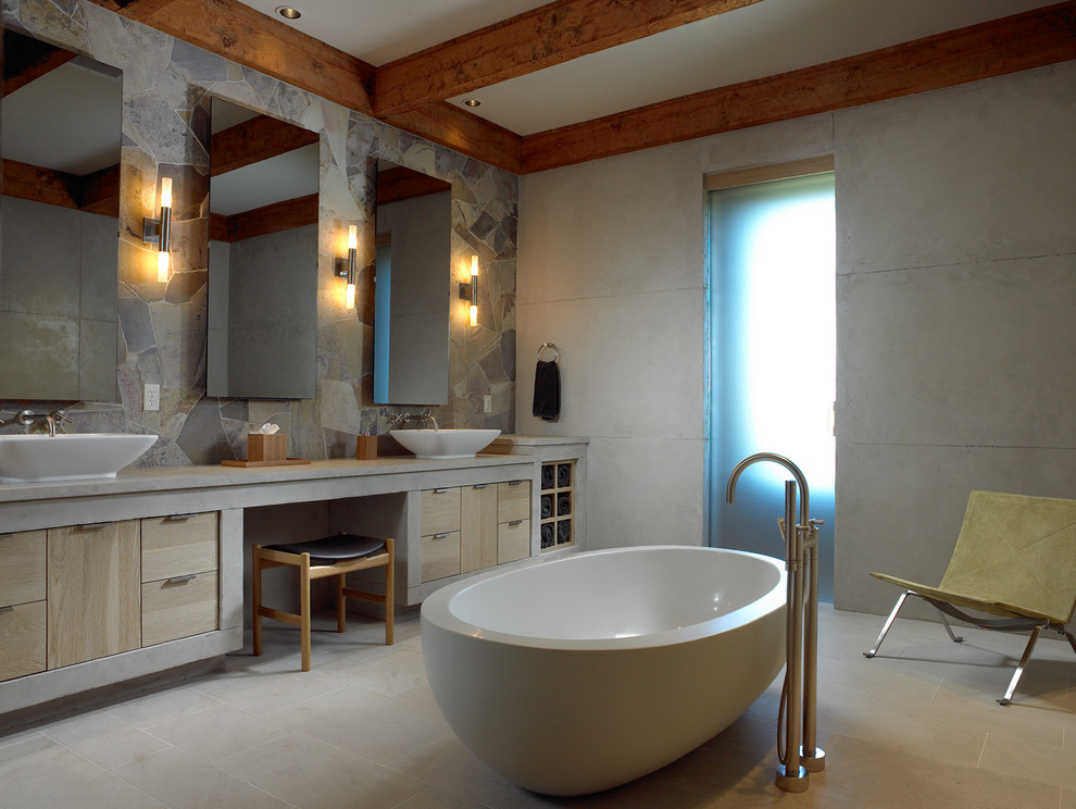 Design ideas for a mid-sized country master bathroom in Other with flat-panel cabinets, light wood cabinets, a freestanding tub, a curbless shower, a vessel sink, grey walls, multi-coloured tile, slate, ceramic floors, concrete benchtops, beige floor and an open shower.