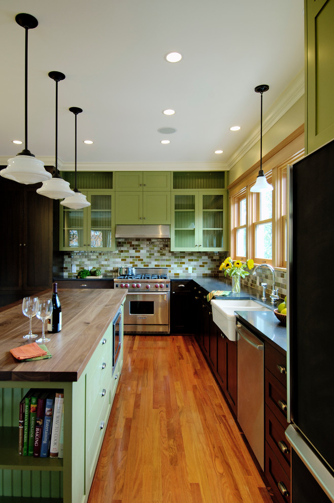 This is an example of a traditional l-shaped kitchen in Seattle with a farmhouse sink, glass-front cabinets, green cabinets, green splashback, subway tile splashback, stainless steel appliances and wood benchtops.
