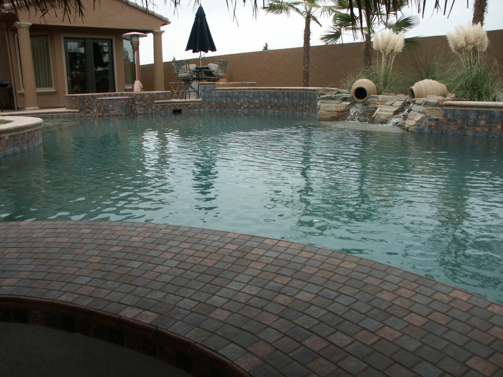 Mid-sized tropical backyard custom-shaped natural pool in Other with stamped concrete and a hot tub.