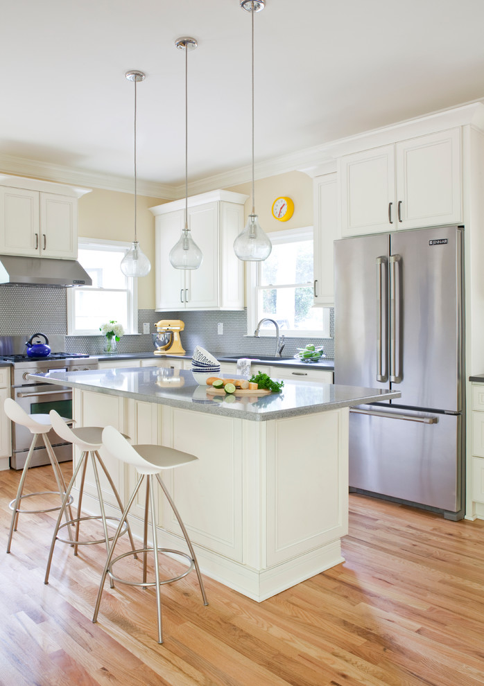 Open concept kitchen - mid-sized transitional l-shaped light wood floor and beige floor open concept kitchen idea with an undermount sink, recessed-panel cabinets, white cabinets, concrete countertops, gray backsplash, mosaic tile backsplash, stainless steel appliances, an island and gray countertops