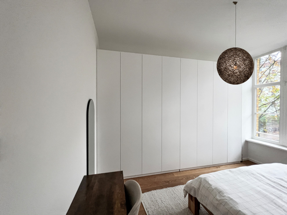 Photo of a mid-sized scandinavian gender-neutral storage and wardrobe in Berlin with flat-panel cabinets, white cabinets, light hardwood floors and brown floor.