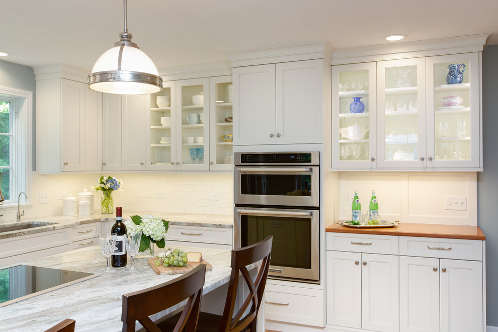 Inspiration for a transitional l-shaped light wood floor eat-in kitchen remodel in Boston with an undermount sink, recessed-panel cabinets, white cabinets, quartzite countertops, white backsplash, subway tile backsplash, stainless steel appliances and an island