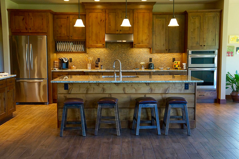 This is an example of a mid-sized country l-shaped eat-in kitchen in Denver with an undermount sink, shaker cabinets, medium wood cabinets, granite benchtops, brown splashback, mosaic tile splashback, stainless steel appliances, medium hardwood floors, with island and brown floor.