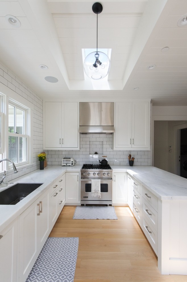 Design ideas for a transitional u-shaped kitchen in San Francisco with an undermount sink, shaker cabinets, white cabinets, white splashback, subway tile splashback, stainless steel appliances, light hardwood floors and a peninsula.
