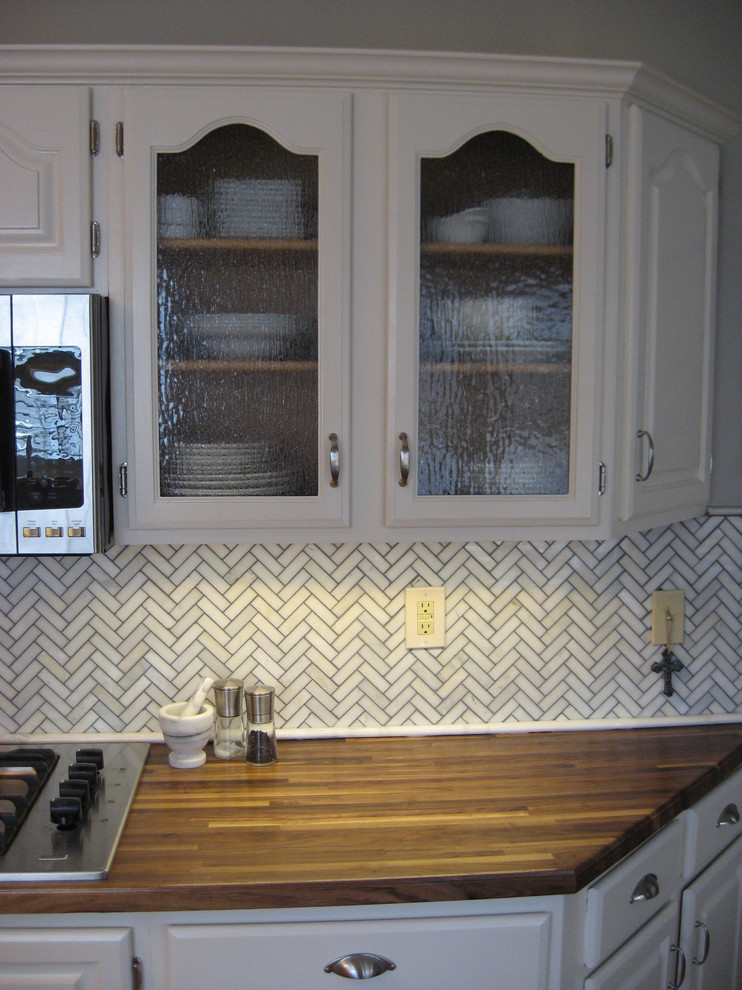 Inspiration for a mid-sized transitional galley light wood floor eat-in kitchen remodel with an undermount sink, raised-panel cabinets, white cabinets, wood countertops, white backsplash, stone tile backsplash, stainless steel appliances and no island