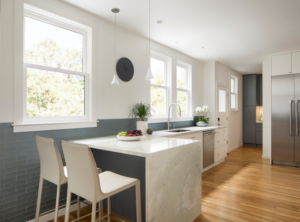 Medium sized contemporary l-shaped kitchen/diner in San Francisco with a submerged sink, flat-panel cabinets, white cabinets, marble worktops, grey splashback, metro tiled splashback, stainless steel appliances, medium hardwood flooring, a breakfast bar, multi-coloured floors and white worktops.