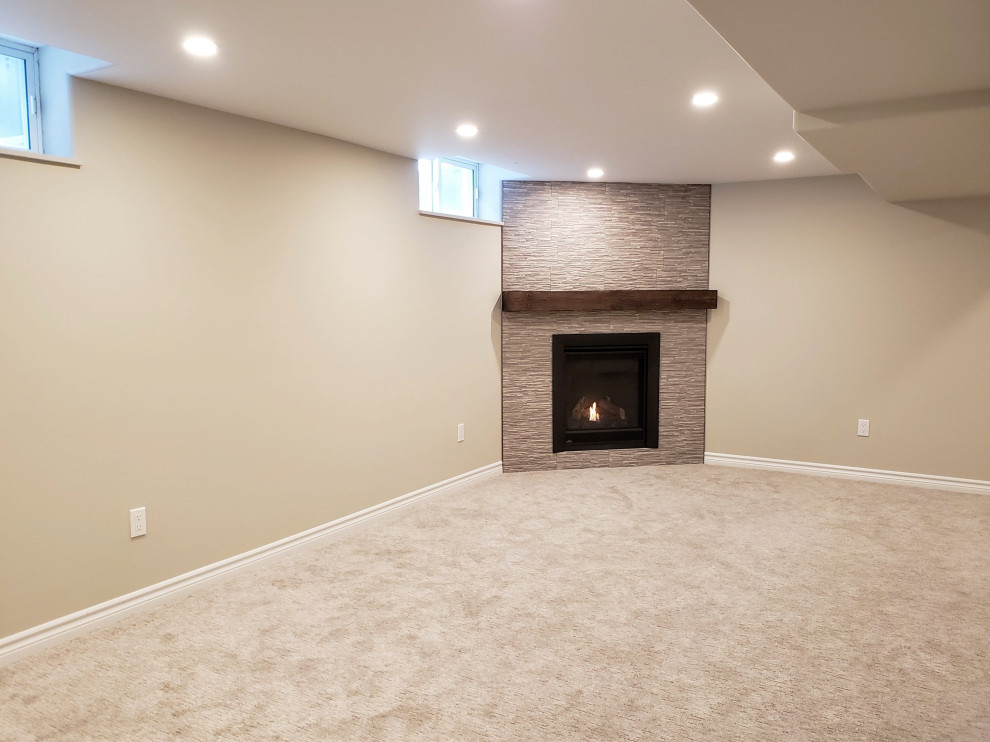 Mid-sized transitional look-out basement in Toronto with beige walls, carpet, a corner fireplace, a tile fireplace surround and grey floor.