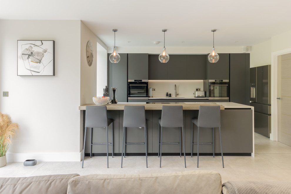 Mid-sized contemporary single-wall open plan kitchen in Other with an integrated sink, flat-panel cabinets, grey cabinets, white splashback, panelled appliances, porcelain floors, with island, beige floor and white benchtop.
