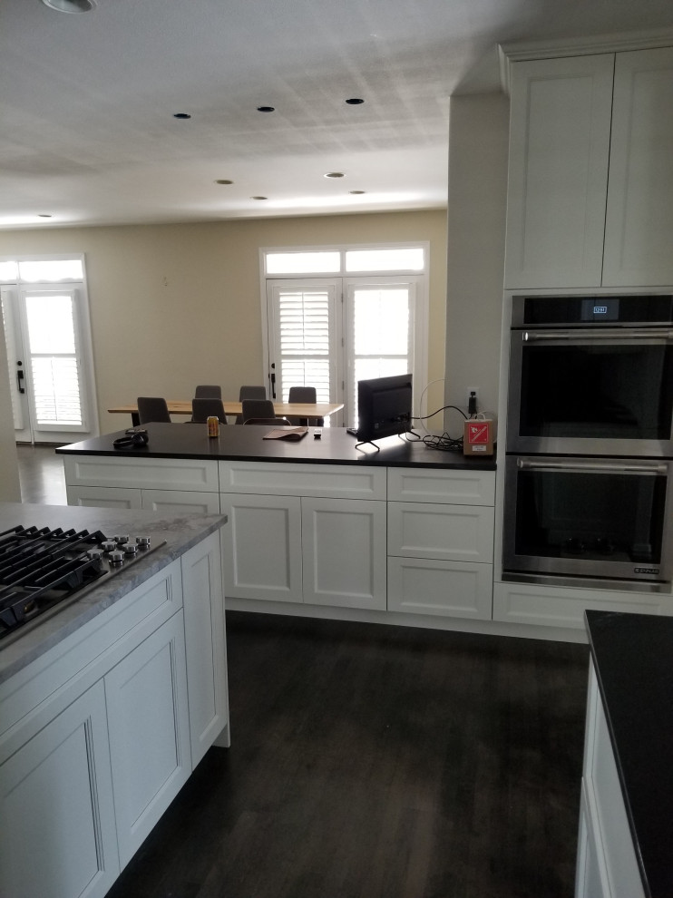 Example of a large transitional u-shaped dark wood floor and brown floor eat-in kitchen design in Denver with an undermount sink, shaker cabinets, white cabinets, quartz countertops, stainless steel appliances, an island and black countertops