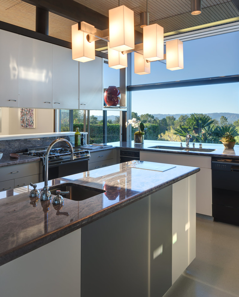 Midcentury u-shaped kitchen in Los Angeles with an undermount sink, flat-panel cabinets, white cabinets, granite benchtops, brown splashback, stone slab splashback, black appliances, with island and brown benchtop.