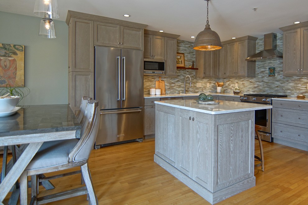 Example of a mid-sized transitional l-shaped medium tone wood floor and beige floor eat-in kitchen design with an undermount sink, beaded inset cabinets, distressed cabinets, marble countertops, gray backsplash, ceramic backsplash, stainless steel appliances, an island and white countertops