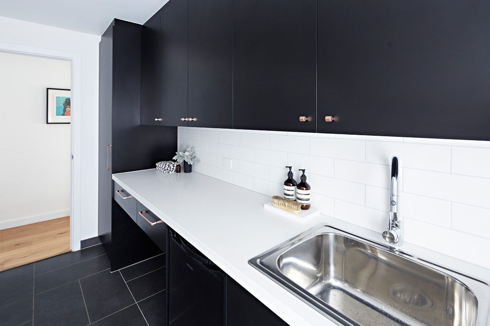 Design ideas for a mid-sized modern single-wall dedicated laundry room in Melbourne with an undermount sink, black cabinets, a stacked washer and dryer, black floor, white benchtop, quartz benchtops and white walls.