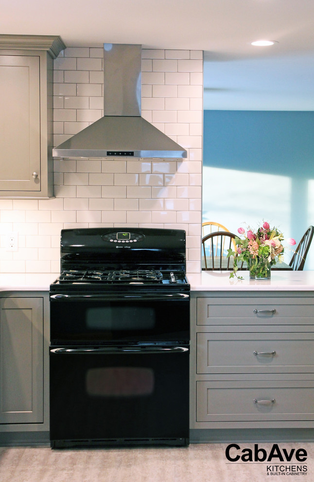 Example of a small transitional l-shaped laminate floor and gray floor enclosed kitchen design with a farmhouse sink, recessed-panel cabinets, gray cabinets, quartz countertops, white backsplash, subway tile backsplash, stainless steel appliances and a peninsula