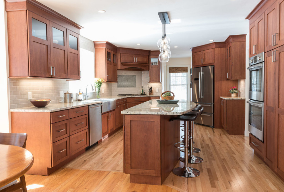 Photo of a mid-sized transitional galley eat-in kitchen in Boston with a farmhouse sink, shaker cabinets, medium wood cabinets, granite benchtops, grey splashback, subway tile splashback, stainless steel appliances, medium hardwood floors, with island, brown floor and beige benchtop.