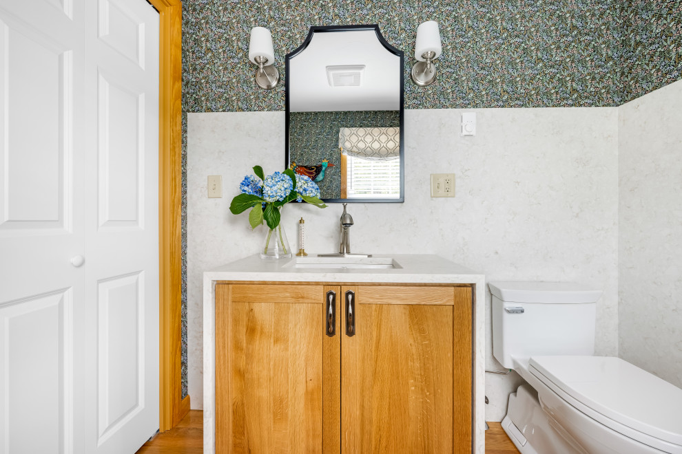 Inspiration for a small traditional cloakroom in Providence with shaker cabinets, medium wood cabinets, a one-piece toilet, multi-coloured walls, medium hardwood flooring, a submerged sink, quartz worktops, beige worktops, a built in vanity unit and wallpapered walls.