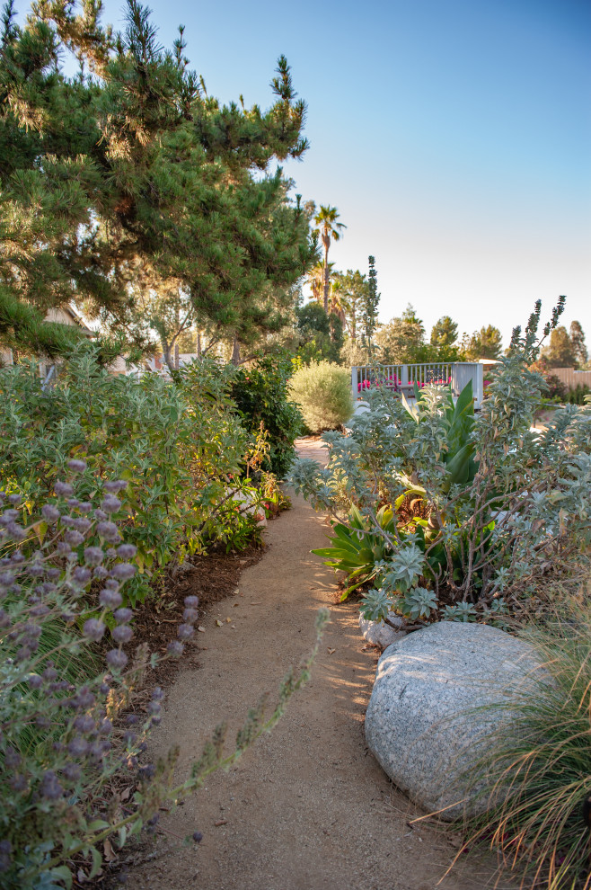 ロサンゼルスにある巨大な、夏のエクレクティックスタイルのおしゃれな裏庭 (ゼリスケープ、庭への小道、半日向、真砂土舗装、樹脂フェンス) の写真