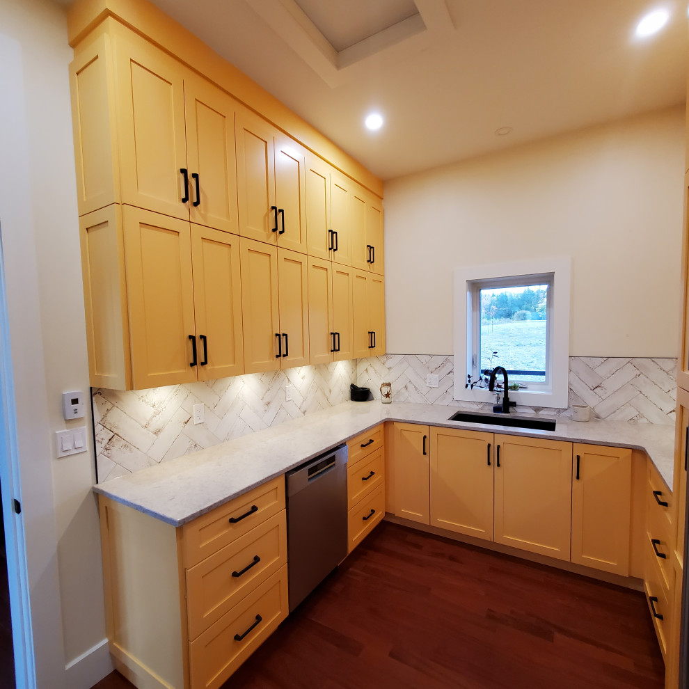 This is an example of a large modern u-shaped kitchen pantry in Other with an undermount sink, shaker cabinets, yellow cabinets, solid surface benchtops, white splashback, subway tile splashback, stainless steel appliances, medium hardwood floors, brown floor and white benchtop.