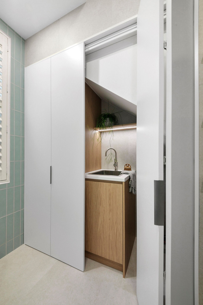 Large modern single-wall utility room in Sydney with a drop-in sink, open cabinets, light wood cabinets, laminate benchtops, grey splashback, ceramic splashback, grey walls, ceramic floors, a stacked washer and dryer, beige floor, white benchtop and vaulted.