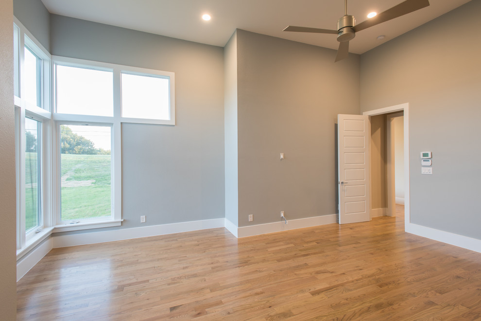 This is an example of a large transitional master bedroom in Dallas with grey walls and light hardwood floors.