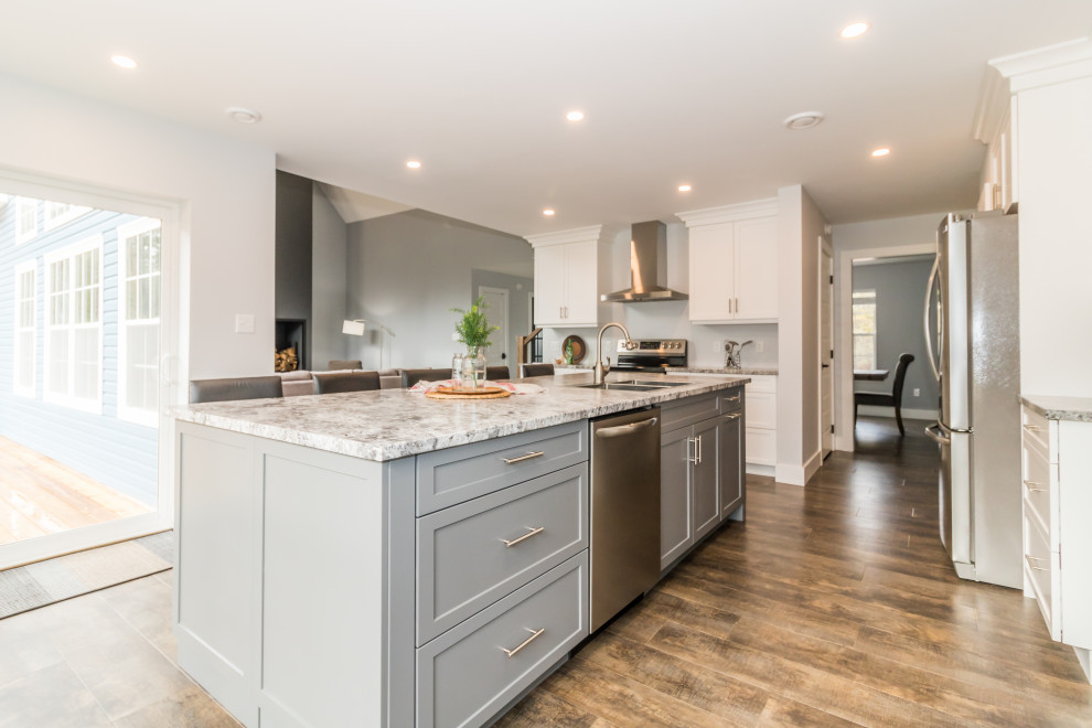 Large l-shaped brown floor and vinyl floor kitchen photo with blue cabinets, stainless steel appliances, an island, multicolored countertops, a drop-in sink, recessed-panel cabinets and laminate countertops
