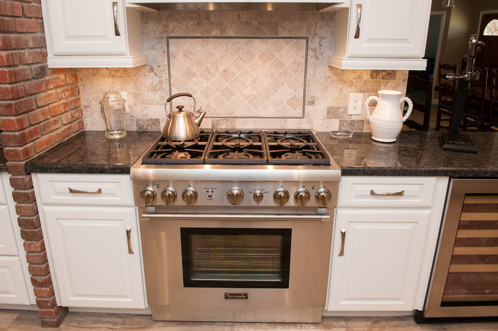 Mid-sized transitional galley porcelain tile and beige floor enclosed kitchen photo with a triple-bowl sink, raised-panel cabinets, white cabinets, granite countertops, beige backsplash, porcelain backsplash, stainless steel appliances and a peninsula