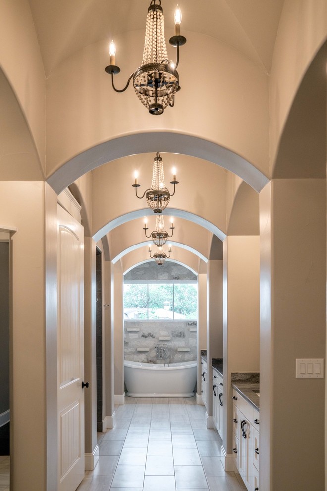 This is an example of a large transitional master bathroom in Austin with shaker cabinets, white cabinets, a freestanding tub, beige tile, stone tile, beige walls, porcelain floors, granite benchtops and beige floor.