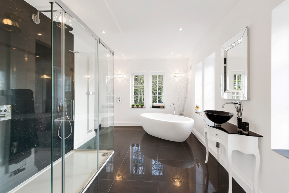 Large contemporary master bathroom in West Midlands with white cabinets, a freestanding tub, black tile, white walls, porcelain floors, a console sink, glass benchtops, black floor, a corner shower, a sliding shower screen and flat-panel cabinets.