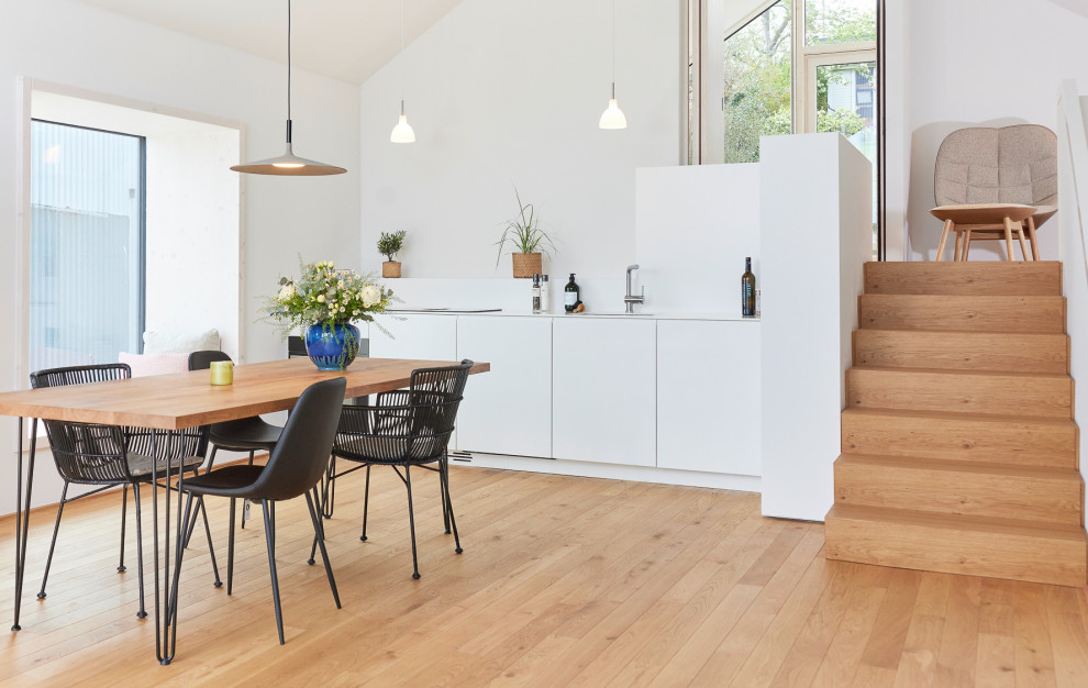 Photo of a small scandinavian single-wall open plan kitchen in Hamburg with an integrated sink, flat-panel cabinets, white cabinets, solid surface benchtops, white splashback, panelled appliances, no island, white benchtop, glass sheet splashback and light hardwood floors.
