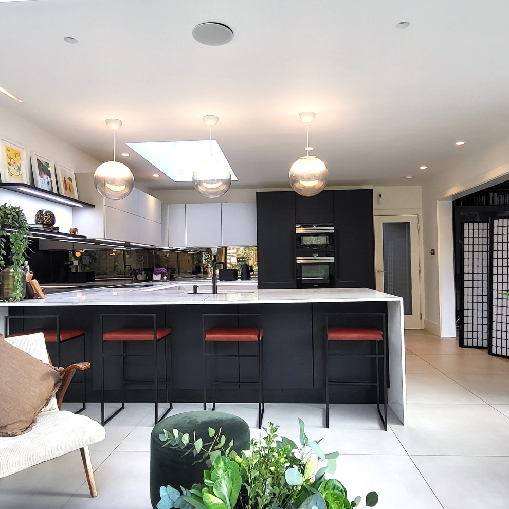 Design ideas for a large contemporary u-shaped eat-in kitchen in Essex with an undermount sink, recessed-panel cabinets, beige cabinets, marble benchtops, mirror splashback, black appliances, porcelain floors, a peninsula, beige floor and yellow benchtop.