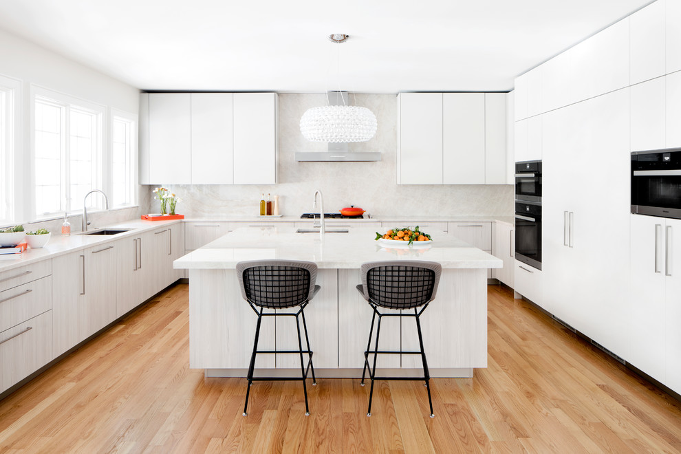 This is an example of a large contemporary u-shaped kitchen in DC Metro with an undermount sink, flat-panel cabinets, quartzite benchtops, stone slab splashback, black appliances, with island, white cabinets, white splashback and light hardwood floors.